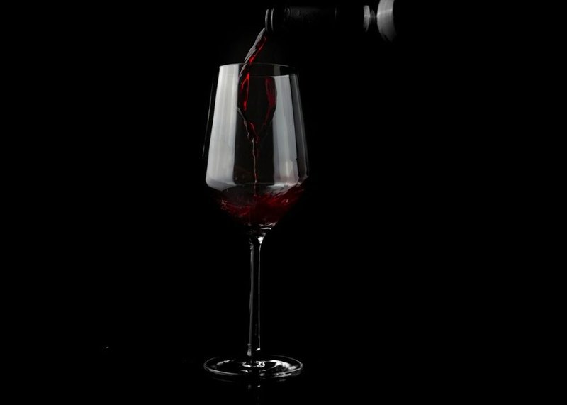 Weinglas vor schwarzem Hintergrund wird mit Rotwein gefüllt